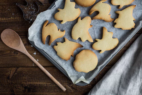 Best fall treats - Halloween cookies on parchment paper on a baking sheet. A wooden spoon lays next to the baking sheet.