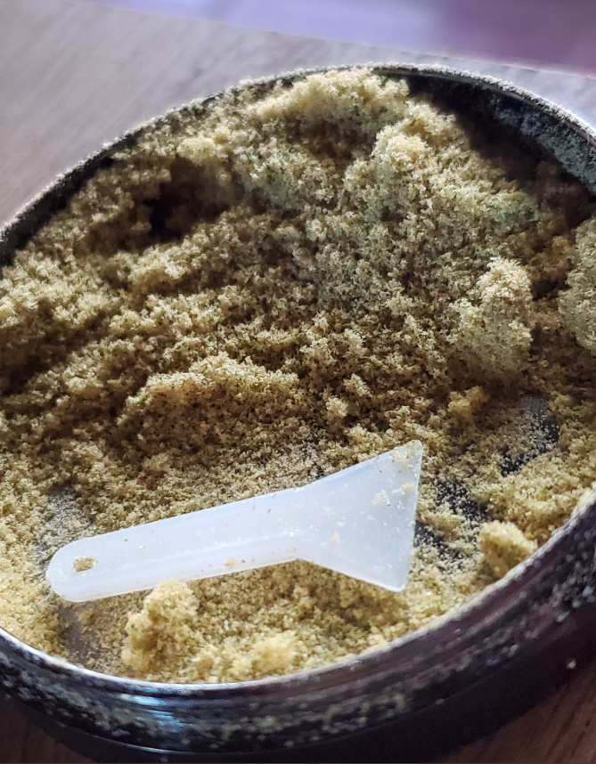 Kief in a grinder with a white kief scraper 